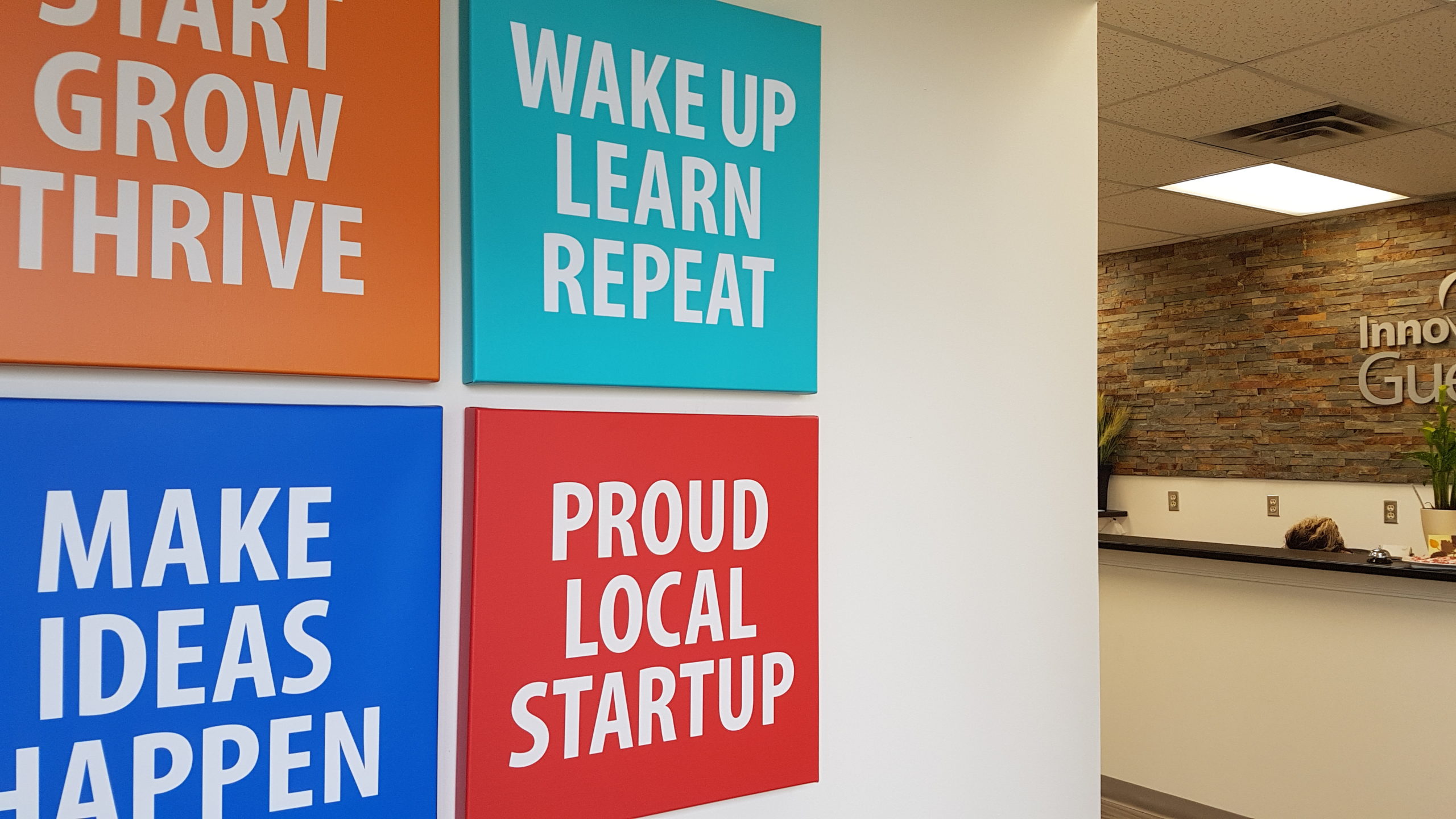 interior office of innovation guelph. Motivational signs on the wall say Proud Local Start up, wake up learn repeat, make ideas happen, start grow thrive.
