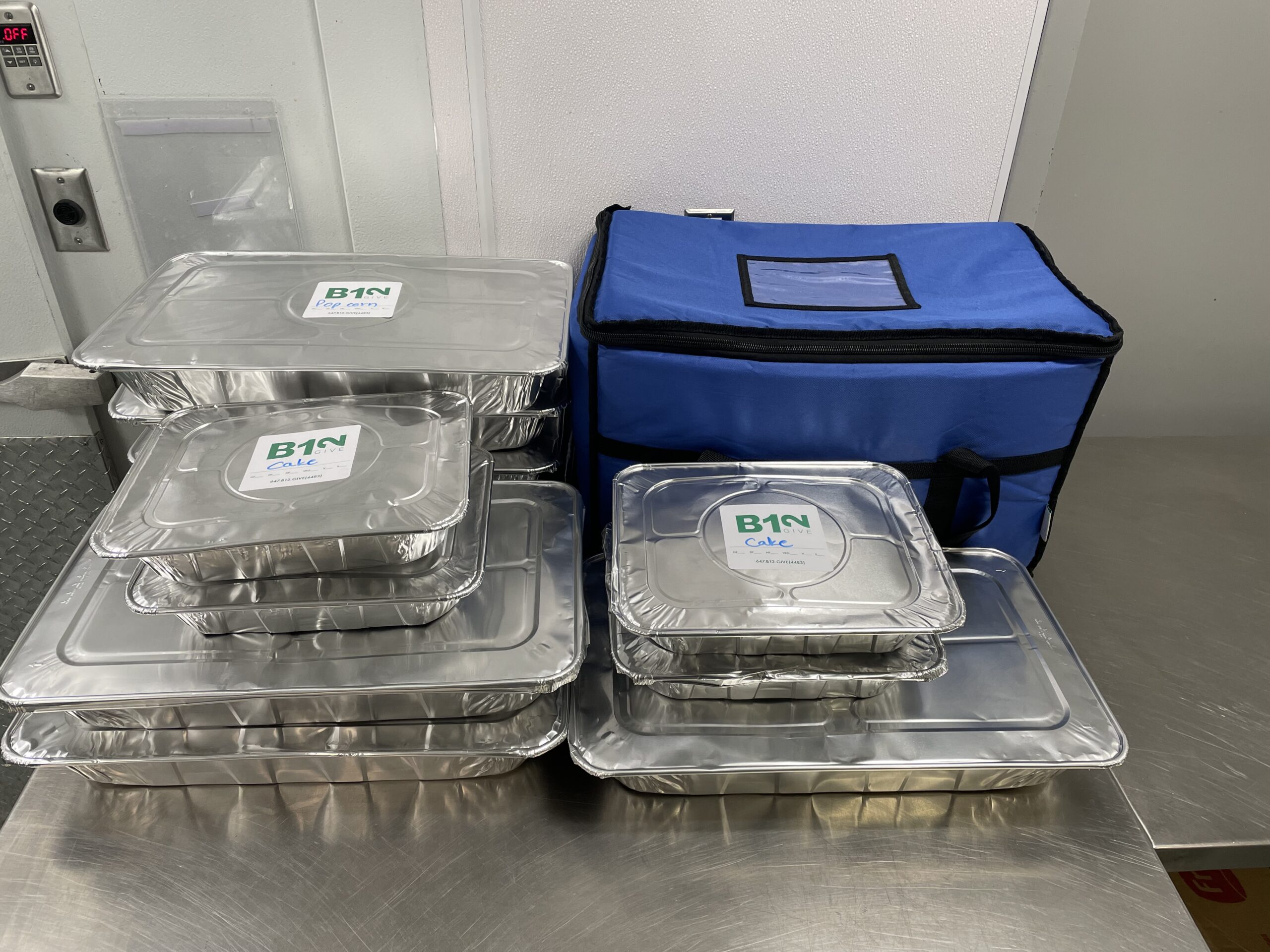 aluminum trays of food with blue cooler bag on a kitchen prep table