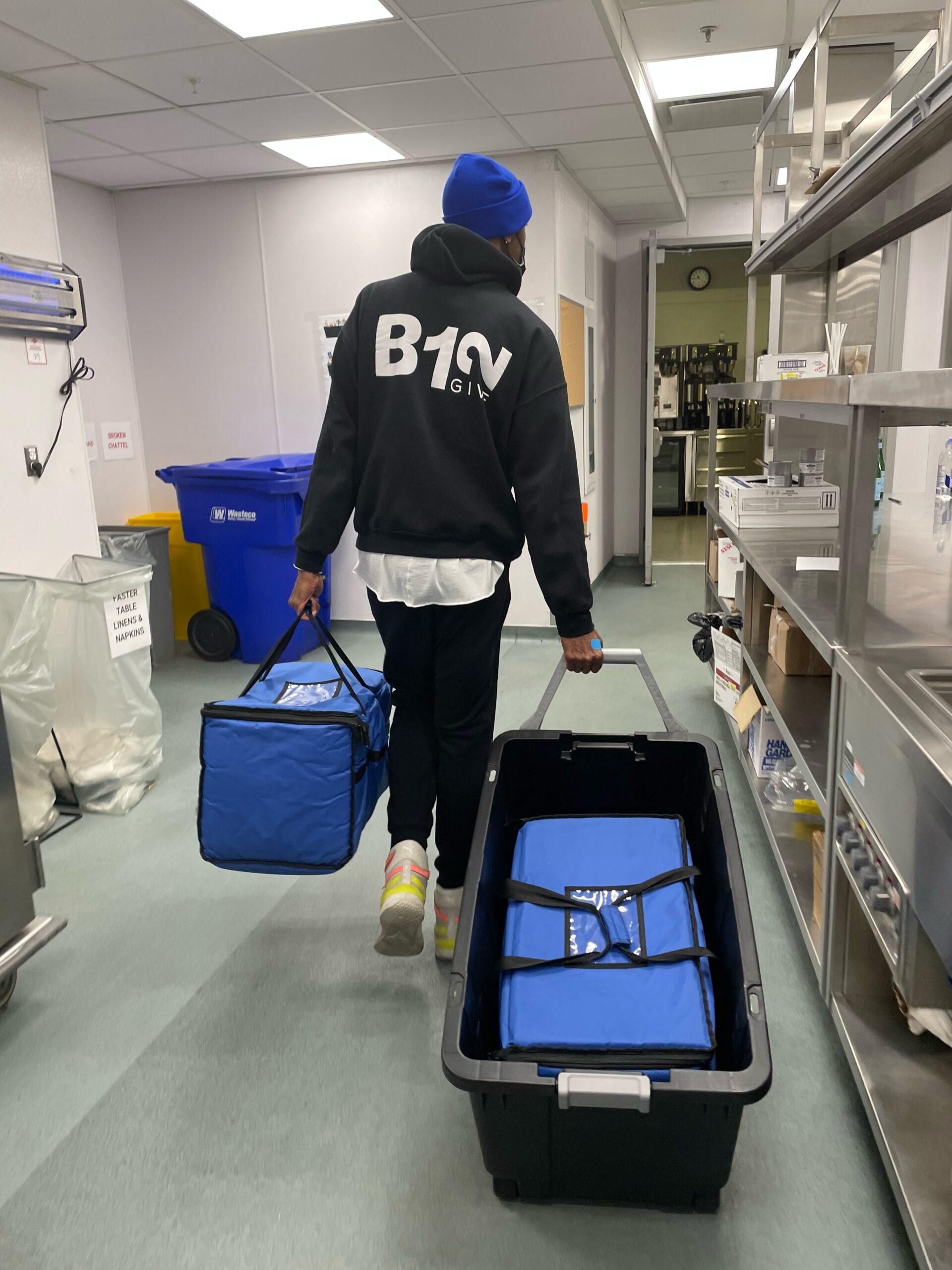 man carrying blue cooler bag and rolling another bag with B12Give logo